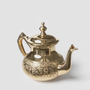 Peut inclure: Une théière dorée avec un couvercle et une poignée. La théière présente un motif en relief orné autour de la base et un bec verseur. La théière est en métal et a une finition brillante.