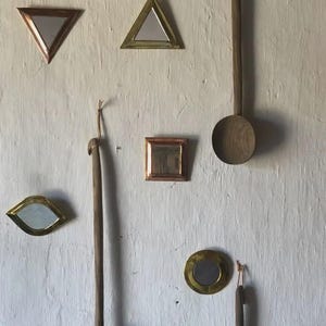 Peut inclure: Une collection de miroirs décoratifs de différentes formes, dont des triangles, des carrés et des cercles, avec des cadres métalliques. Des cuillères en bois sont suspendues à côté des miroirs sur un mur blanc texturé.