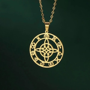 May include: A gold-coloured pendant necklace. The circular pendant has an intricate, openwork design with a central knot and surrounding symbols. The necklace hangs from a delicate chain. The pendant is displayed against a dark green background.