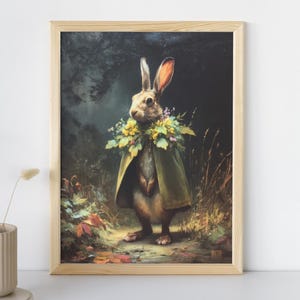May include: A framed art print depicting a rabbit in a green cape and floral collar, set in a forest with autumn leaves and tall grass. The artwork has a vintage, painterly style, with a dark background.