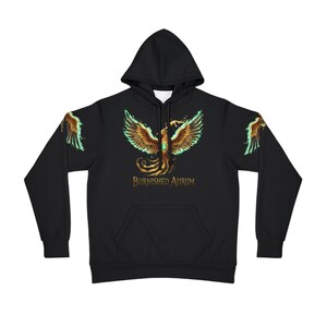 Peut inclure: Sweat à capuche noir avec un motif de phénix doré et des touches de turquoise. Le phénix est centré, avec des motifs d'ailes sur les manches. Le texte "BURNISHED AURUM" est en dessous.
