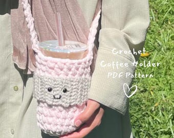 May include: A handmade crochet coffee holder in light pink and white, with a small face design. The holder has a strap and is designed to carry a beverage cup with a straw. The text "Crochet Coffee Holder PDF Pattern" is visible.
