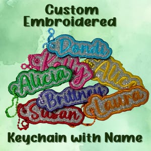 May include: Custom embroidered keychains with names in various colors, including blue, pink, green, yellow, orange, and red. Each keychain features a glittery silver background and a matching border. The text "Custom Embroidered Keychain with Name" is displayed.