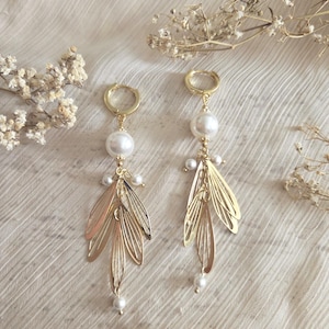 May include: A pair of gold-colored dangle earrings. Each earring features a large white pearl, smaller pearls, and a gold leaf design. The earrings hang from gold hoops.