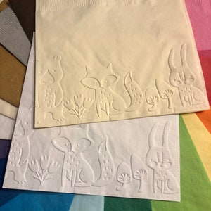 Puede incluir: Dos servilletas de papel blancas con dise&ntilde;os en relieve de animales del bosque. La servilleta superior presenta un oso, un zorro y un conejo, mientras que la servilleta inferior presenta un zorro, un conejo y setas.
