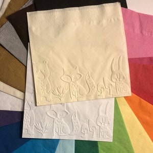 Puede incluir: Un abanico de servilletas de papel de colores con un dise&ntilde;o en relieve de un zorro, un conejo y otras criaturas del bosque. Las servilletas est&aacute;n dispuestas en forma de arco&iacute;ris.