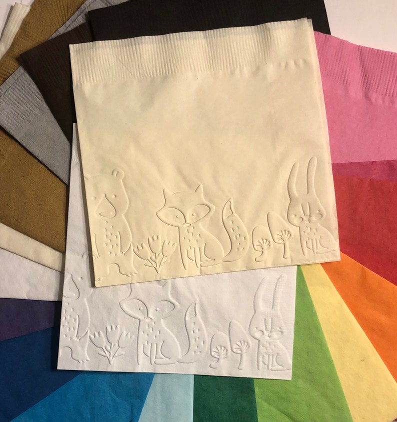 Puede incluir: Un abanico de servilletas de papel de colores con un dise&ntilde;o en relieve de un zorro, un conejo y otras criaturas del bosque. Las servilletas est&aacute;n dispuestas en forma de arco&iacute;ris.