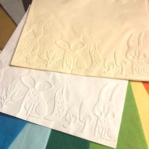 Puede incluir: Dos servilletas de papel blancas con dise&ntilde;os en relieve de animales del bosque. La servilleta superior presenta un conejo, un zorro y dos setas. La servilleta inferior presenta un zorro, un conejo y dos setas.