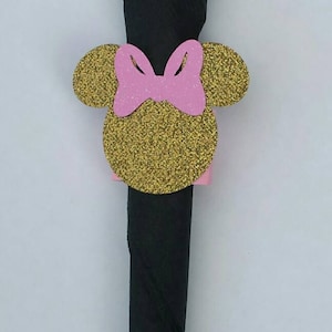 K&ouml;nnte beinhalten: Ein schwarzer Serviettenhalter mit einem goldenen Glitzer-Minnie-Maus-Kopf-Design. Der Kopf hat rosa Ohren und eine rosa Schleife.