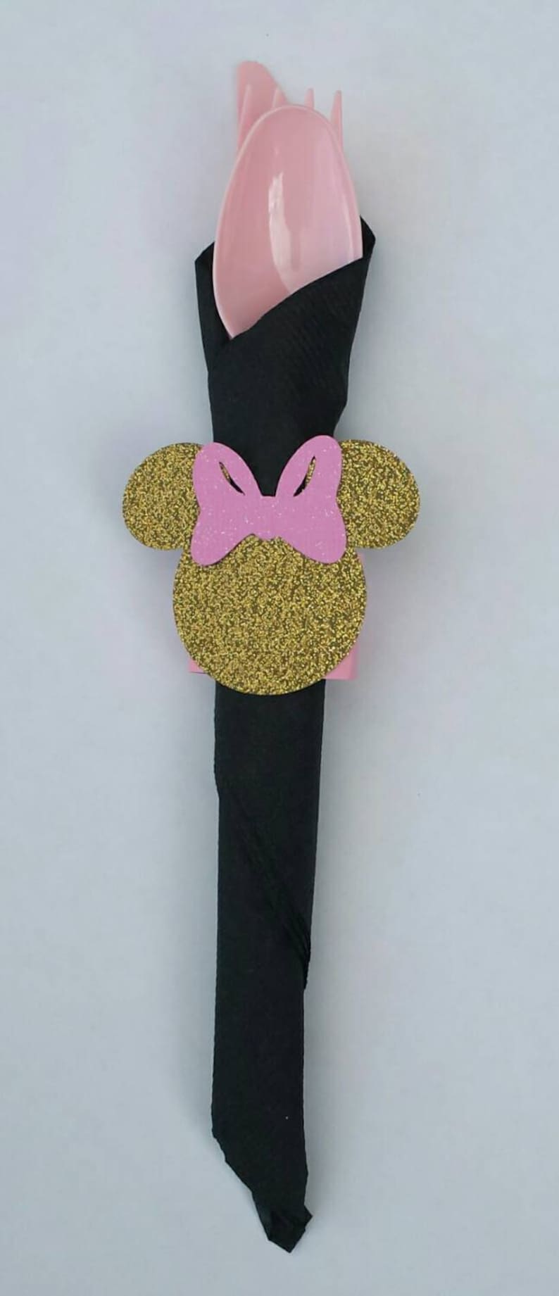 K&ouml;nnte beinhalten: Ein schwarzer Serviettenhalter mit einem goldenen Glitzer-Minnie-Maus-Kopf-Design. Der Kopf hat rosa Ohren und eine rosa Schleife.