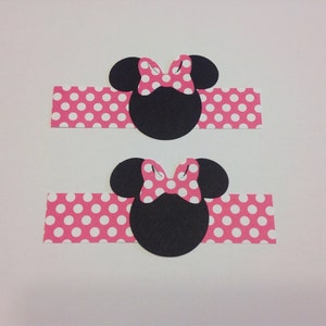 Op de afbeelding: Twee zwarte Minnie Mouse hoofd uitsparingen met roze stippen strikken en bijpassende roze stippen banden. Het ontwerp is een klassiek stripfiguur thema, ideaal voor knutselen of feestversieringen.
