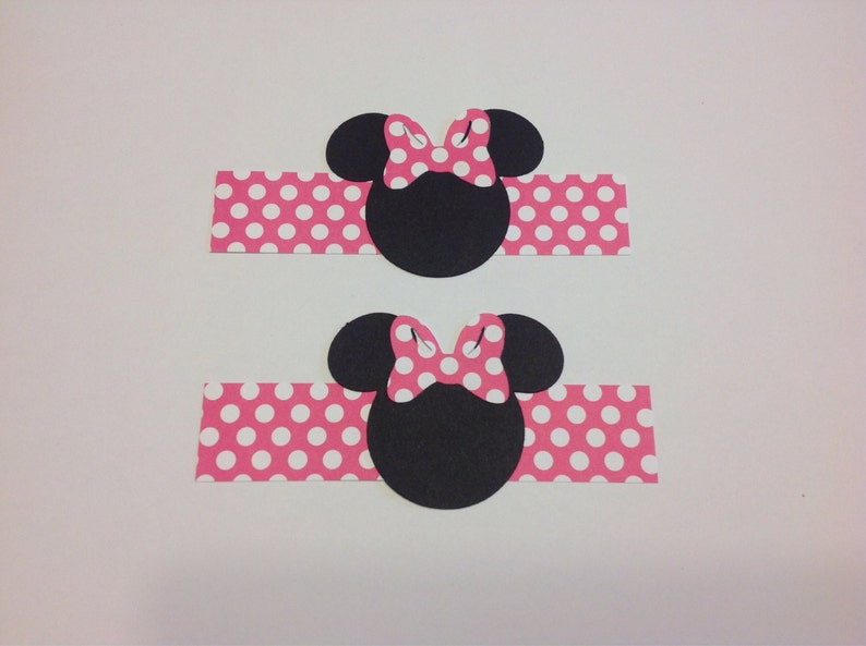 Op de afbeelding: Twee zwarte Minnie Mouse hoofd uitsparingen met roze stippen strikken en bijpassende roze stippen banden. Het ontwerp is een klassiek stripfiguur thema, ideaal voor knutselen of feestversieringen.