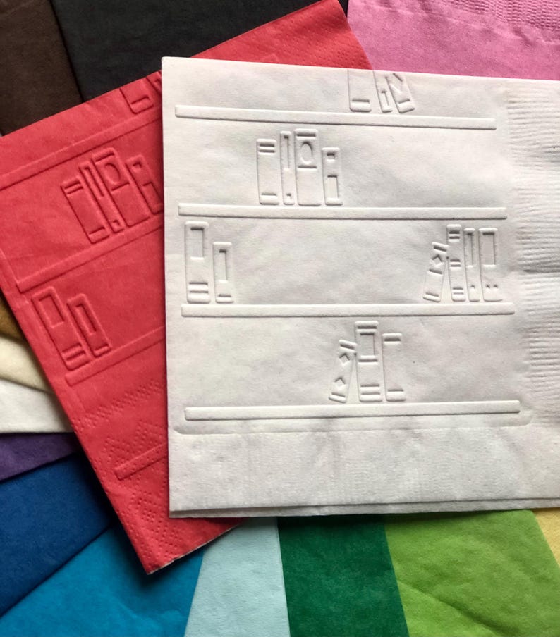 Puede incluir: Una servilleta de papel blanca con un dise&ntilde;o de estanter&iacute;a. La servilleta tiene un patr&oacute;n en relieve de libros en estantes. La servilleta est&aacute; rodeada de otras servilletas de varios colores.