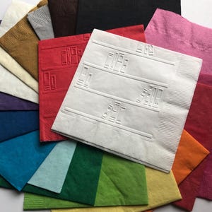 Puede incluir: Una variedad de servilletas de papel de colores, incluyendo rojo, rosa, naranja, verde, azul y blanco. La servilleta blanca tiene un dise&ntilde;o de estanter&iacute;as con libros en ellas.