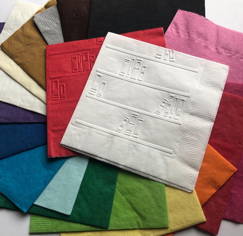 Puede incluir: Una variedad de servilletas de papel de colores, incluyendo rojo, rosa, naranja, verde, azul y blanco. La servilleta blanca tiene un dise&ntilde;o de estanter&iacute;as con libros en ellas.