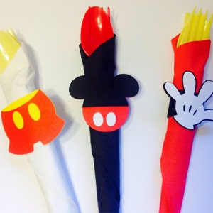 Op de afbeelding: Drie decoratieve servetringen met Mickey Mouse-thema. E&eacute;n heeft een gele broek met twee gele cirkels, een andere een zwarte kop met een rode cirkel en witte cirkels, en de laatste een witte handschoen.