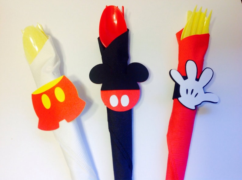 Op de afbeelding: Drie decoratieve servetringen met Mickey Mouse-thema. E&eacute;n heeft een gele broek met twee gele cirkels, een andere een zwarte kop met een rode cirkel en witte cirkels, en de laatste een witte handschoen.