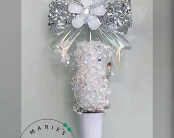 May include: A white pen with a decorative top. The top features clear, sparkling beads, a silver bow, and a white flower. The pen has the text "MARIE'S ESSENTIALS" in a circular logo.