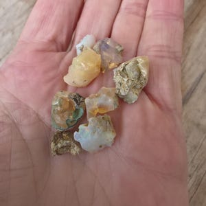 May include: A handful of rough opal gemstones in various colors, including white, yellow, and iridescent flashes of color. The raw stones have a natural, unpolished appearance.
