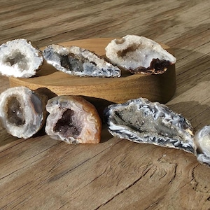 May include: A collection of geode slices with crystal formations in shades of white, gray, and brown. The geodes are displayed on a wooden surface and a small wooden stand. The natural stone formations vary in size and shape.