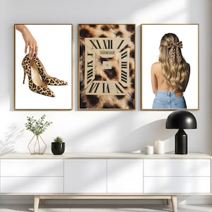 May include: Three framed art prints. The left print features a hand holding a pair of leopard print high heels. The center print has a leopard print background with a clock design. The right print shows a person with a leopard print bow.