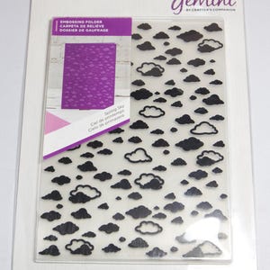 May include: A clear plastic embossing folder with a black design of clouds. The folder is labeled "Spring Sky" and "Ciel de printemps" and "Cielo de primavera". The folder is packaged in a white plastic sleeve with the Gemini logo and the words "By Crafter's Companion".