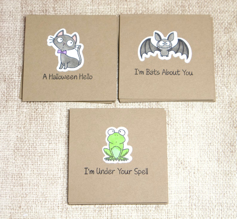 May include: Three square greeting cards with cartoon illustrations. One card features a gray cat with a purple bow tie and the text "A Halloween Hello." Another card has a bat with the text "I'm Bats About You." The third card shows a frog with the text "I'm Under Your Spell."