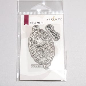 May include: Clear plastic packaging containing a set of three clear rubber stamps. The stamps feature a tulip motif, a decorative frame, and the word "thanks".