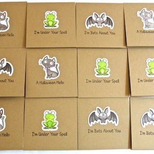 May include: A collection of square, brown cards with Halloween-themed illustrations. Each card features a different design: a cat, a frog, or a bat, with phrases like "A Halloween Hello" and "I'm Bats About You."