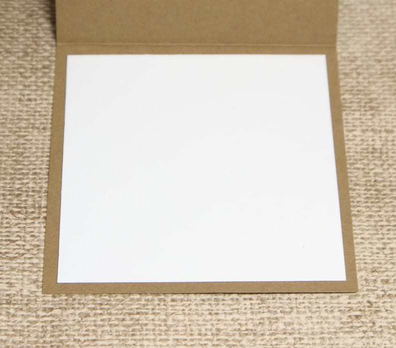 May include: A blank greeting card with a white interior and a brown, textured exterior. The card is open, revealing the blank white space for a personalized message. The card is set against a neutral background.