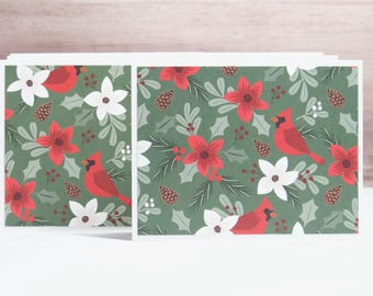 May include: A stack of folded greeting cards featuring a repeating pattern on a dark green background. The design includes red cardinal birds, white and red flowers, brown pinecones, green holly leaves, and small red berries in a festive arrangement.