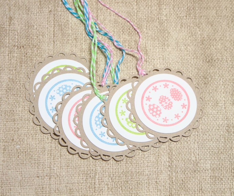 May include: Set of six round gift tags with scalloped edges. Each tag features a different pastel colored floral design with a white background. The tags are tied with twine.