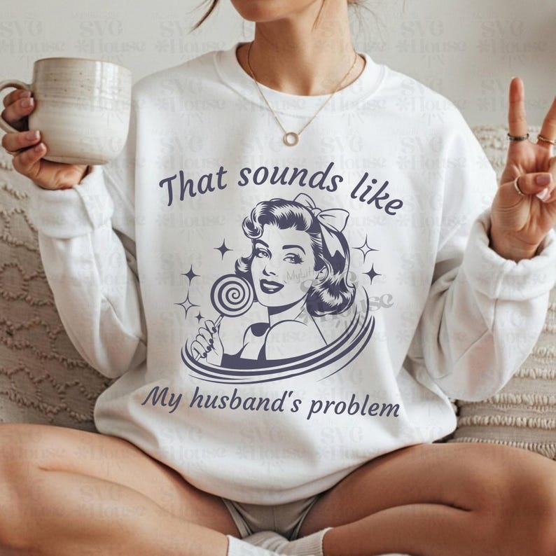 K&ouml;nnte beinhalten: Wei&szlig;es Sweatshirt mit einem Retro-Grafikdesign einer Frau mit einem Lutscher und dem Text "That sounds like My husband's problem". Das Design ist dunkelblau. Das Sweatshirt hat lange &Auml;rmel.