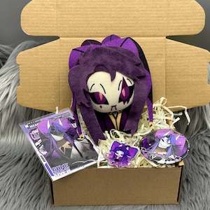 Könnte beinhalten: Geschenkbox mit einer lila Plüschpuppe, einem Schlüsselanhänger, einem Knopf und einem Druck. Die Puppe hat ein weißes Gesicht mit lila Augen und Haaren. Der Aufdruck lautet "GAME OVER". Die Box ist mit Stroh gefüllt.