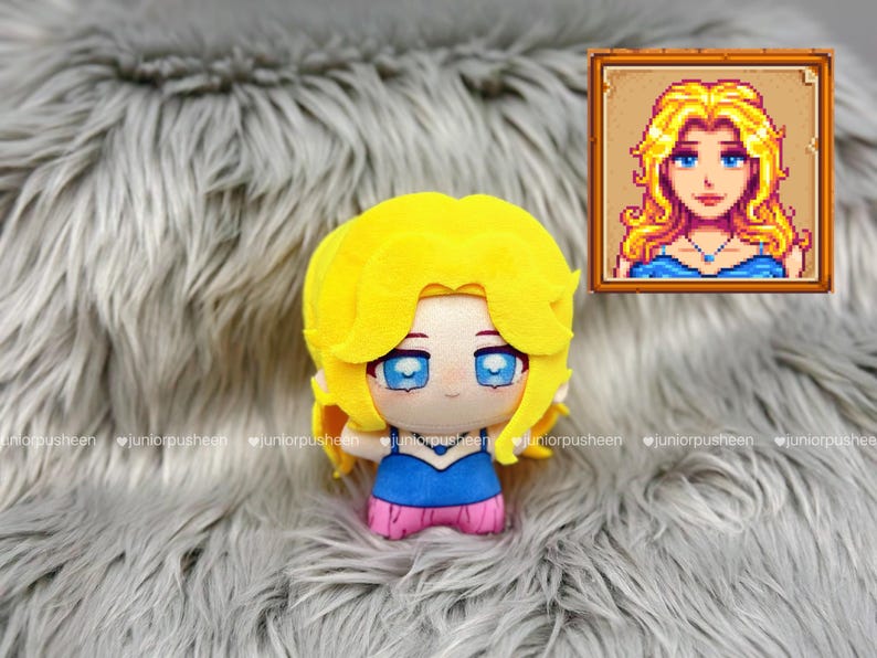 K&ouml;nnte beinhalten: Ein Pl&uuml;schpuppe eines Charakters mit gelben Haaren, blauen Augen und einem blau-rosa Outfit. Die Puppe befindet sich auf einer grauen, pelzigen Oberfl&auml;che. Ein gerahmtes Pixel-Art-Portr&auml;t des Charakters ist im Hintergrund.