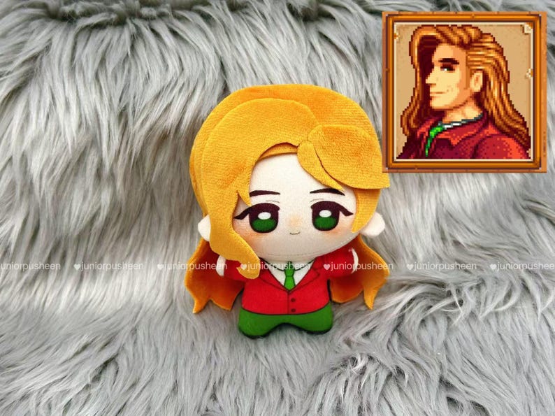 May include: A plush doll of a character with yellow hair, green eyes, and a red jacket with a green tie. The doll is on a grey, fluffy surface. A framed pixel art portrait of the character is in the upper right corner.