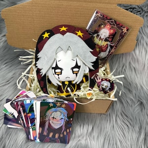 以下が含まれることがあります： ぬいぐるみ、アクリルチャーム、ピンバッジ、カードが入ったギフトボックス。 ぬいぐるみは白い顔、灰色の髪、黒と赤の衣装です。 カードには笑顔のキャラクターが描かれています。 ふわふわの灰色の表面にあります。
