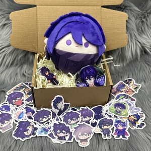 Puede incluir: Un peluche con pelo morado y una mascarilla a juego est&aacute; en una caja de cart&oacute;n con pegatinas y un pin. Las pegatinas y el pin presentan un personaje con pelo morado. La caja est&aacute; llena de papel triturado.