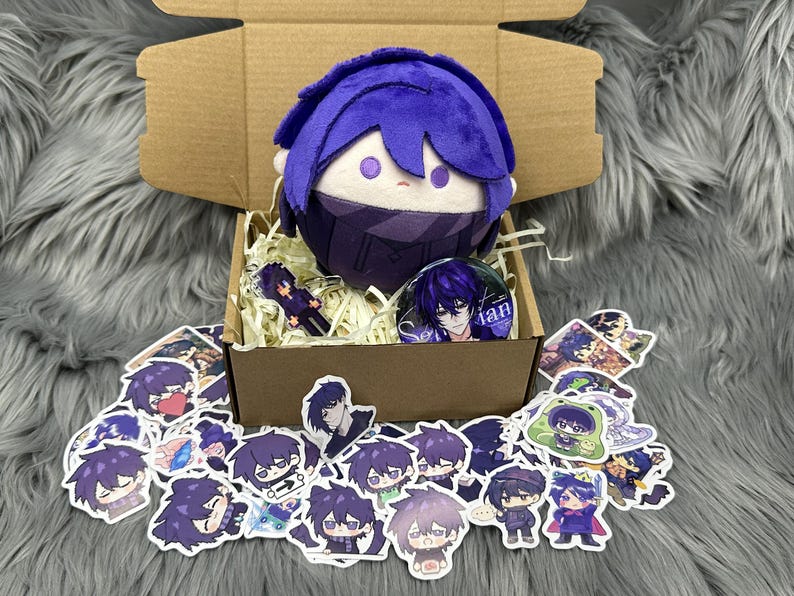 Puede incluir: Un peluche con pelo morado y una mascarilla a juego est&aacute; en una caja de cart&oacute;n con pegatinas y un pin. Las pegatinas y el pin presentan un personaje con pelo morado. La caja est&aacute; llena de papel triturado.