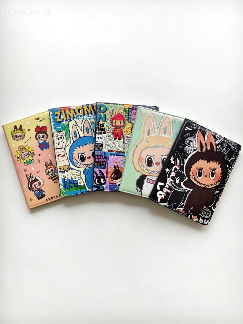 May include: Five rectangular passport holders arranged in a fan shape. Each features a unique graphic print of cartoon characters with rabbit ears, including text like ZIMOMO and LABUBU, in various colors such as peach, blue, green, and black.