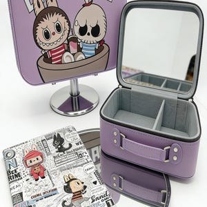 May include: A lavender rectangular vanity case with a top handle and a Labubu character graphic. An open matching case reveals a grey interior with a mirror and dividers. A flat rectangular notebook features black and white comic book illustrations.