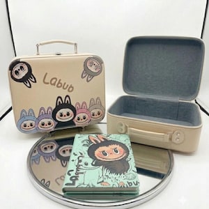 May include: Two beige rectangular storage cases with top handles and a light green notebook. The cases feature cartoon character illustrations and the text Labub. One case is closed, and the other is open, revealing a grey interior lining.