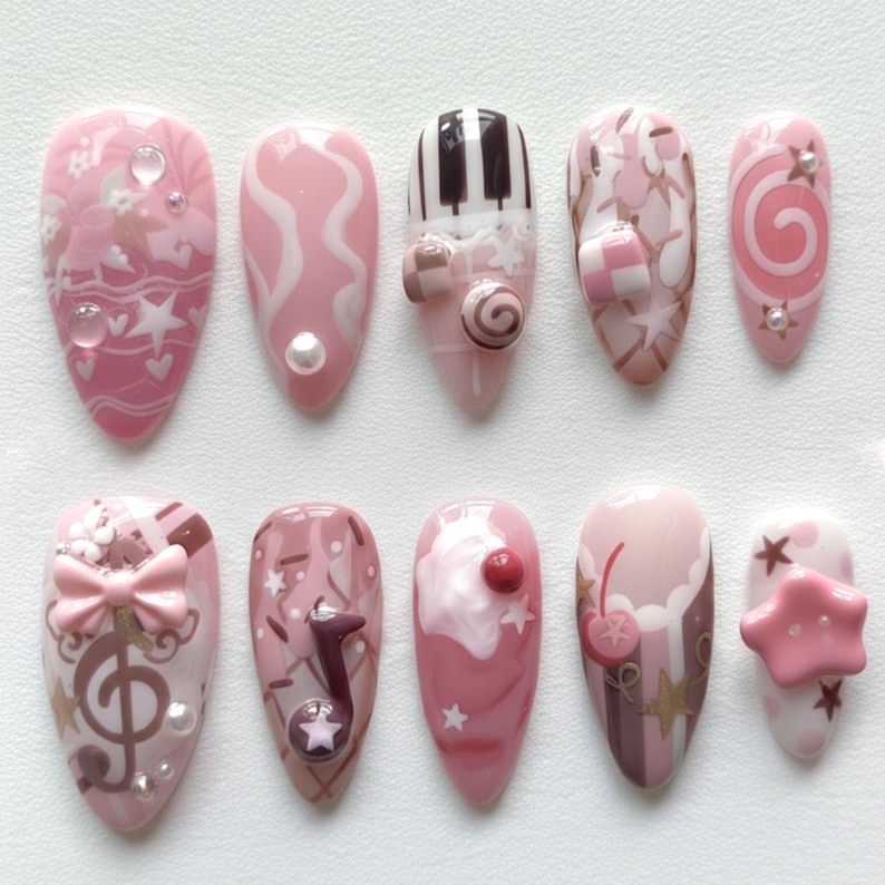 May include: A set of ten pink and white artificial nails with various designs. The designs include swirls, musical notes, piano keys, bows, and candy. Some nails feature 3D embellishments like pearls and stars. The nails are oval-shaped.