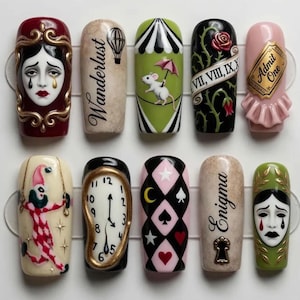 May include: A set of ten press-on nails featuring intricate hand-painted designs including a crying face in a gold frame, the word Wanderlust with a hot air balloon, a mouse on a tightrope, Roman numerals, an Admit One ticket, a jester, a melting clock, playing card suits, the word Enigma with a keyhole, and a sad mask.