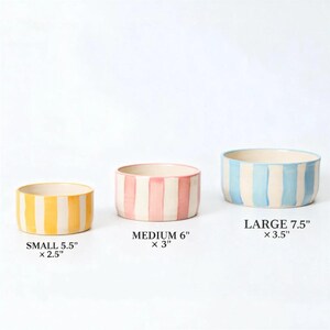 K&ouml;nnte beinhalten: Drei Keramikschalen mit vertikalen Streifen in Gelb, Rosa und Blau. Die kleine Schale ist 14 cm x 6,4 cm, die mittlere Schale ist 15,2 cm x 7,6 cm und die gro&szlig;e Schale ist 19 cm x 8,9 cm. Jede Schale hat einen cremefarbenen Innenraum.