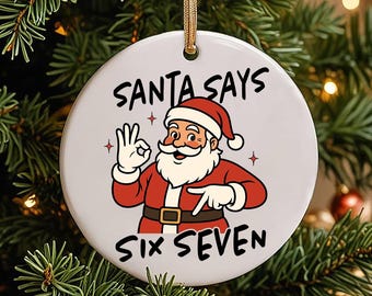 May include: A round, white Christmas ornament with a gold ribbon for hanging. The ornament features a cartoon Santa Claus illustration and the text "SANTA SAYS SIX SEVEN". The Santa illustration is in red and white, with a white beard and gloves.