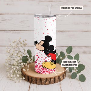 May include: A white tumbler with a silver lid and a plastic-free straw. The tumbler features a cartoon image of Mickey Mouse kissing, surrounded by red heart shapes. The text "Fits in Most Cupholders!" is also visible.