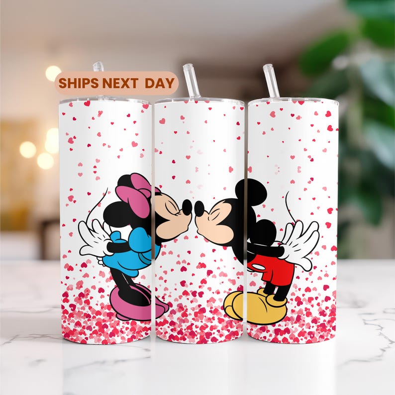 May include: Three white tumblers featuring Mickey and Minnie Mouse kissing, with a red heart pattern and a straw. The text "SHIPS NEXT DAY" is on a tan banner. Each tumbler is approximately 20 cm tall.