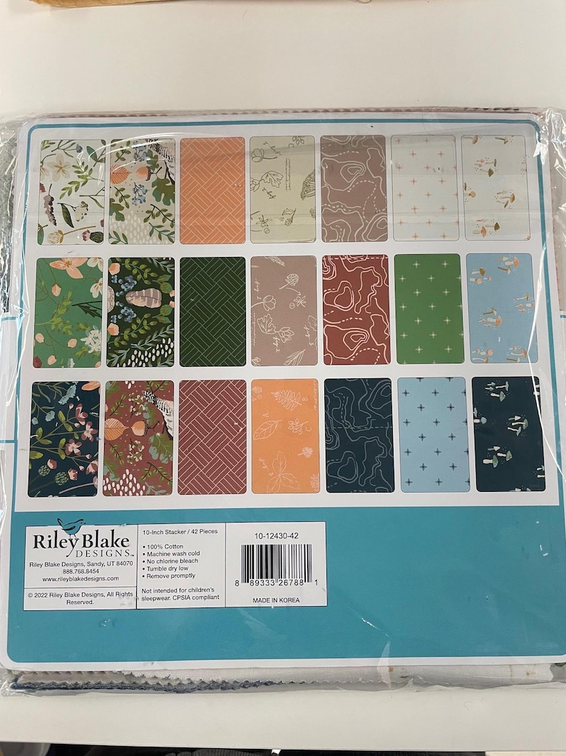 May include: A 10-inch stacker of 42 fabric pieces with various patterns, including floral, geometric, and map designs. The color palette includes greens, oranges, and blues. The Riley Blake Designs product is made of 100% cotton.
