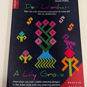May include: A softcover book titled Der Lilienhain and A Lily Grove by Claudia Wollny. The dark blue cover features colorful pixelated floral and geometric motifs, with text detailing over 100 tablet weaving designs in the Arlon style.